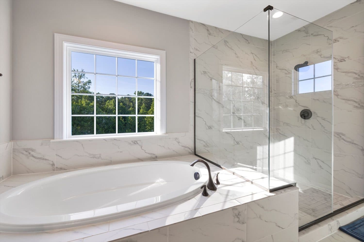 Salle de bain lumineuse avec baignoire, douche vitrée et grande fenêtre.