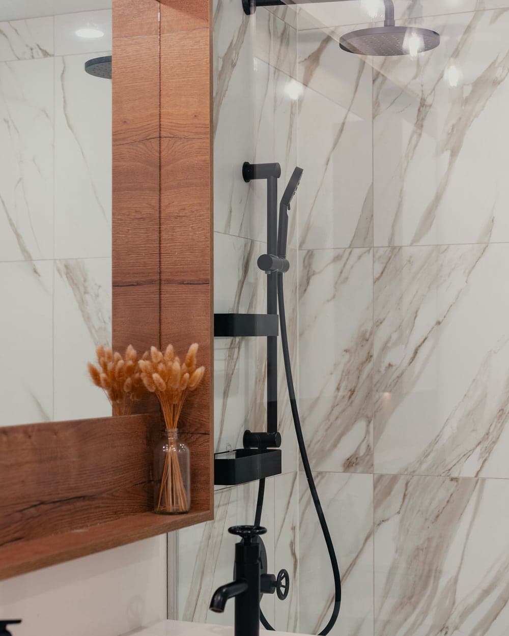 Vanité de salle de bain en bois avec robinetterie noire et douche vitrée en arrière-plan.