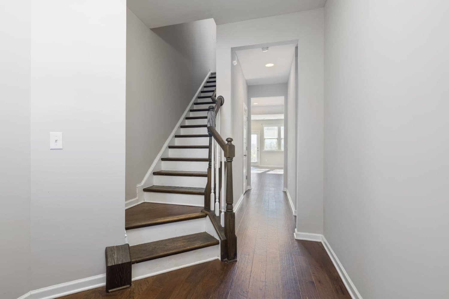 Hall résidentiel lumineux avec plancher de bois, escalier et ouvertures.